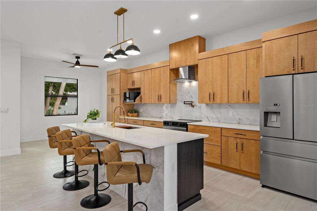 A modern kitchen features light wood cabinetry, a marble-topped island, and three tan barstools — 10928 OSCEOLA DRIVE, NEW PORT RICHEY, FL