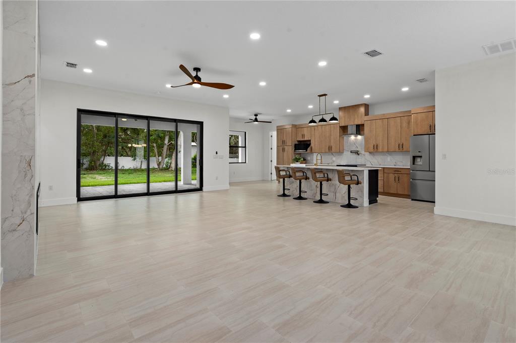 An open-concept kitchen and living area features light tile floors, wood cabinetry, and sliding doors — 10928 OSCEOLA DRIVE, NEW PORT RICHEY, FL