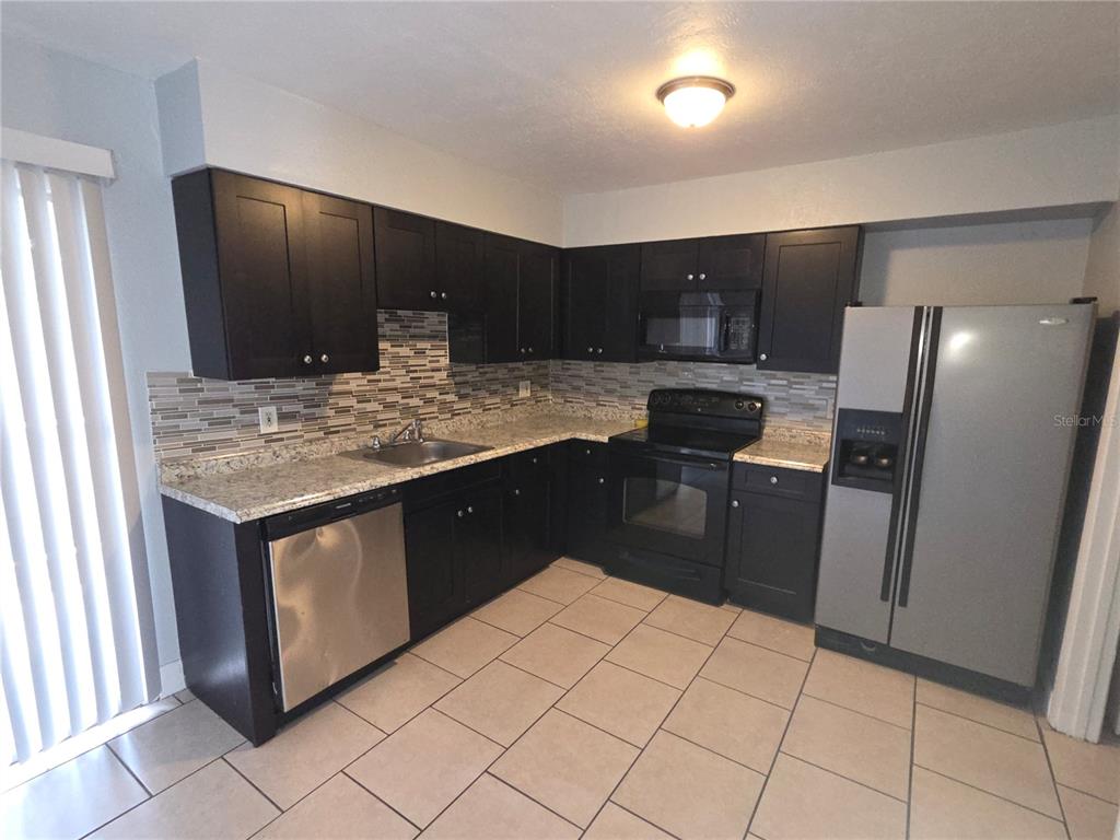 A kitchen features dark cabinets, granite countertops, stainless steel appliances, and light-colored tile flooring — 4001 WOODFERN DRIVE UNIT C1, ORLANDO, FL