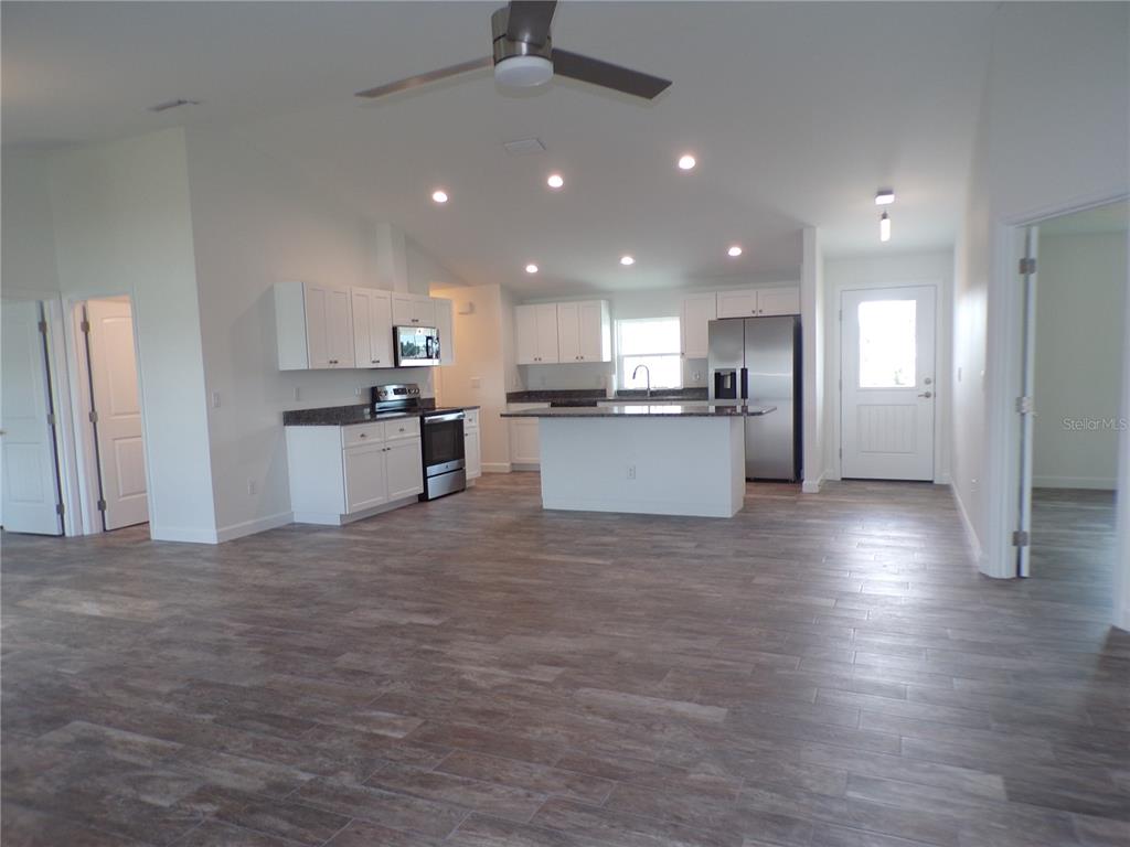 A kitchen with white cabinets, stainless steel appliances, and an island features wood-look tile flooring — 3308 PORT CHARLOTTE BOULEVARD, PORT CHARLOTTE, FL