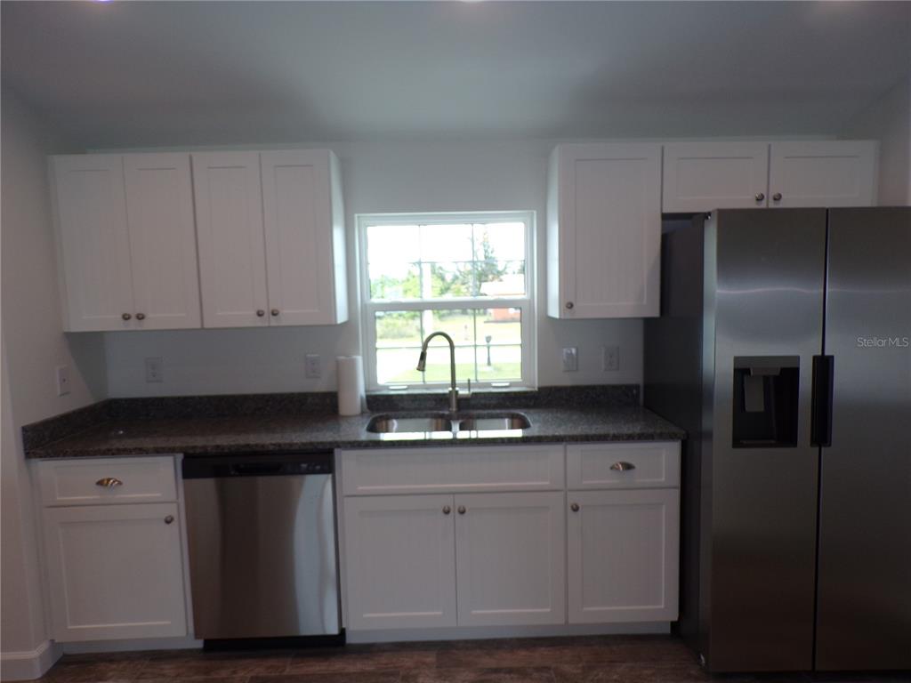 A kitchen features white cabinets, granite countertops, a stainless steel dishwasher, and a refrigerator — 3308 PORT CHARLOTTE BOULEVARD, PORT CHARLOTTE, FL