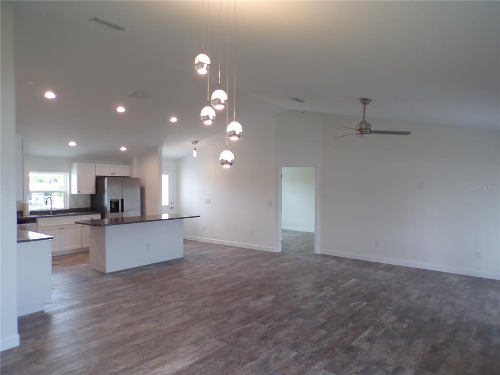 An open-concept kitchen and living area features white cabinets, a kitchen island, and wood-look flooring — 3308 PORT CHARLOTTE BOULEVARD, PORT CHARLOTTE, FL