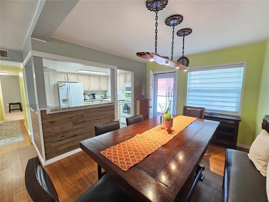 A dining room features a wooden table, a rustic light fixture, and a kitchen pass-through — 5896 PALM LANE UNIT C27, BRADENTON, FL