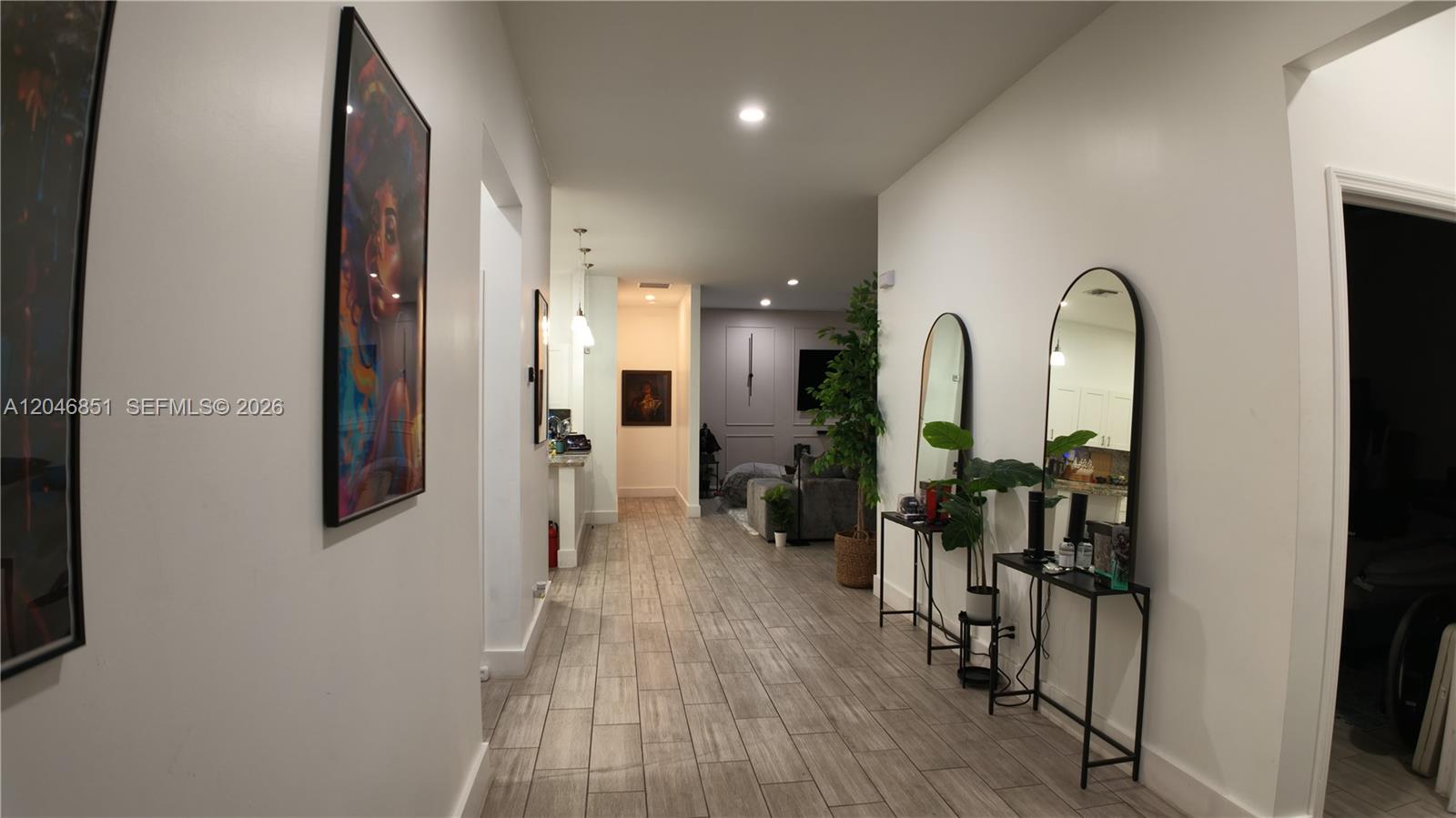 A hallway with wood-look tile flooring leads to a living area featuring arched mirrors — 1831 SW 48th Ave, West Park FL 33023, WEST PARK, FL