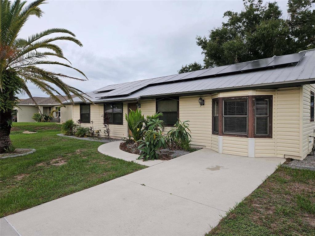 A single-story house with light yellow siding, a metal roof with solar panels, and a driveway — 6270 SPINNAKER BOULEVARD, ENGLEWOOD, FL