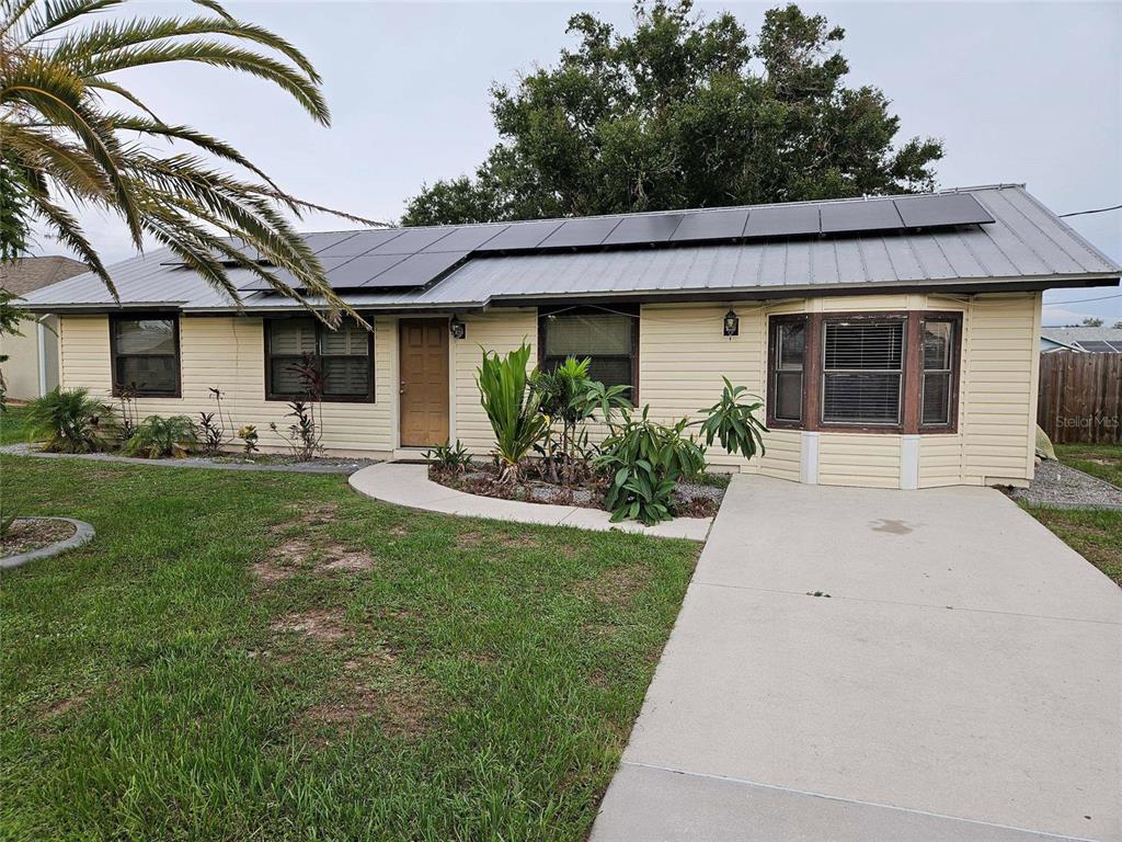 A single-story house with light yellow siding, a metal roof, and solar panels — 6270 SPINNAKER BOULEVARD, ENGLEWOOD, FL