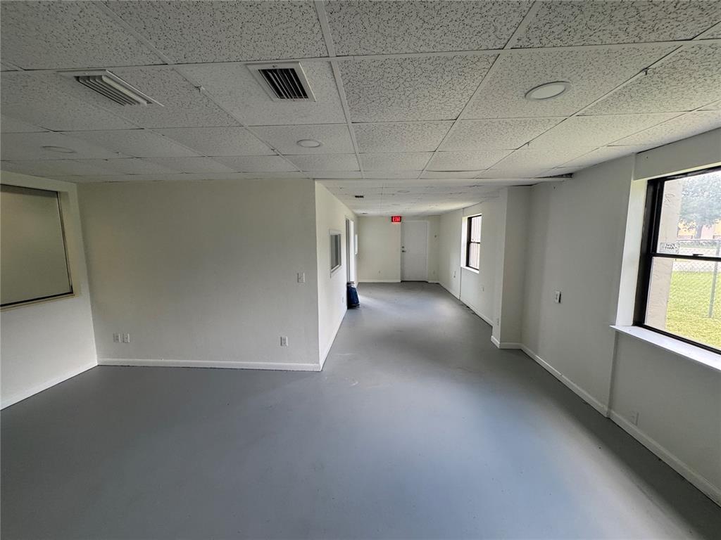 An empty office space features white walls, gray flooring, a drop ceiling, and several windows — 702 W PARK AVENUE UNIT A1, EDGEWATER, FL