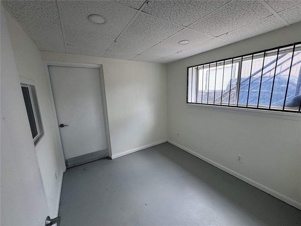 A small room with gray painted floors, white walls, a drop ceiling, and a barred window — 702 W PARK AVENUE UNIT A1, EDGEWATER, FL