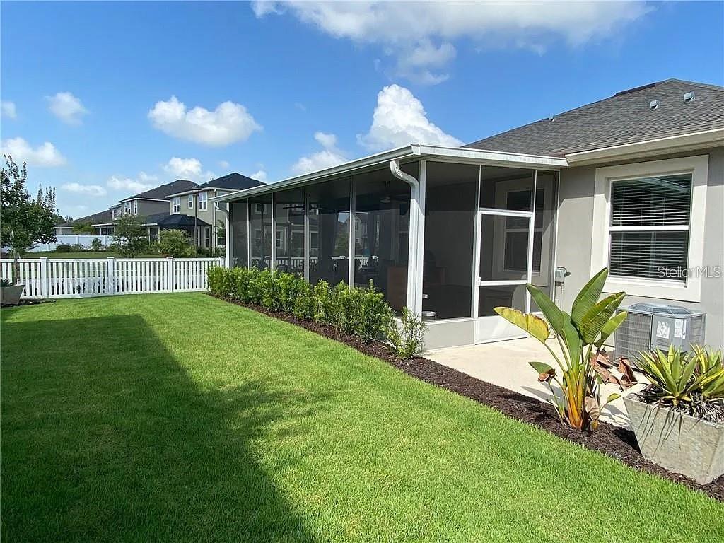 A backyard features a green lawn, a white fence, and a screened-in patio area — 7902 CORKFIELD AVENUE, ORLANDO, FL