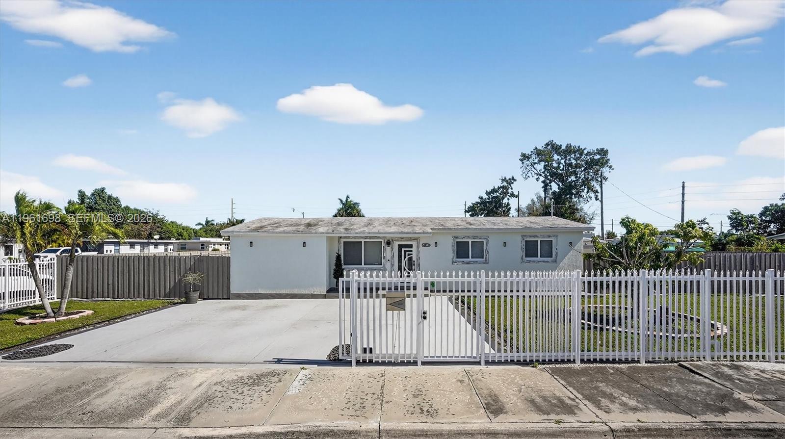 A single-story white house features a concrete driveway and a white picket fence — 22301 SW 117th Pl, Miami FL 33170, MIAMI, FL