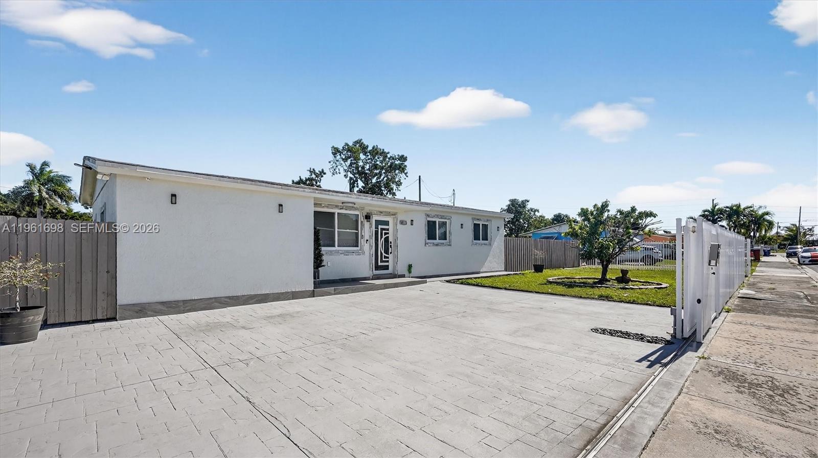 A white single-story house features a large paved driveway and a fenced front yard — 22301 SW 117th Pl, Miami FL 33170, MIAMI, FL