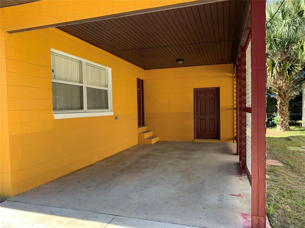 A covered concrete carport features bright yellow block walls and two dark brown doors — 612 KENSINGTON STREET, EUSTIS, FL