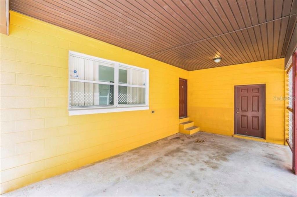 A covered concrete patio features bright yellow block walls, a brown door, and a window — 612 KENSINGTON STREET, EUSTIS, FL