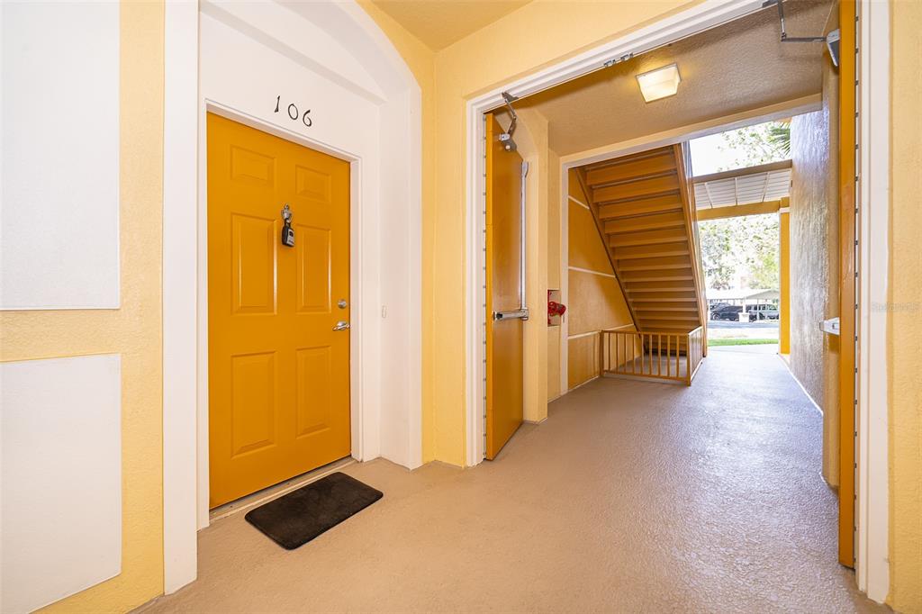 An apartment entrance with a yellow door numbered 106 next to an outdoor stairwell — 3338 ROBERT TRENT JONES DRIVE UNIT 106, ORLANDO, FL