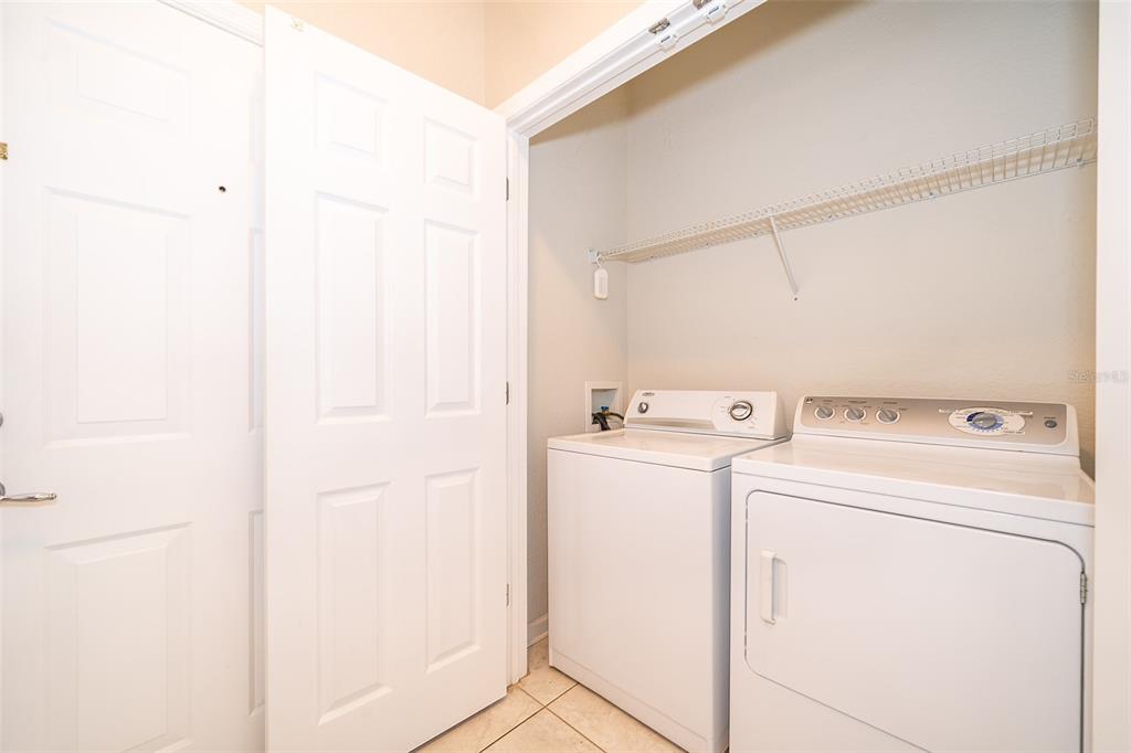 A laundry closet contains a white washer and dryer beneath a wire storage shelf — 3338 ROBERT TRENT JONES DRIVE UNIT 106, ORLANDO, FL