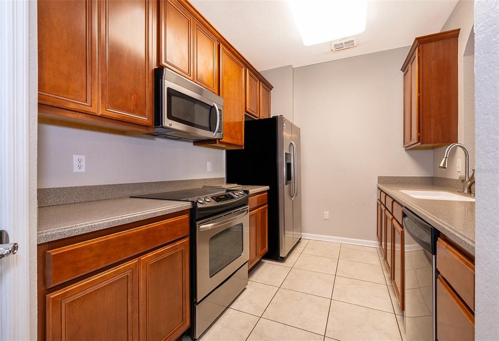 A galley kitchen features wood cabinets, stainless steel appliances, and light-colored tile flooring — 3338 ROBERT TRENT JONES DRIVE UNIT 106, ORLANDO, FL