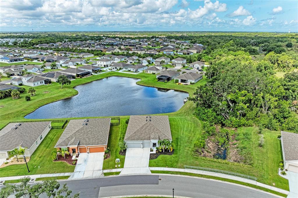 An aerial view shows suburban houses surrounding a central pond near a wooded area — 6421 114TH AVENUE E, PARRISH, FL