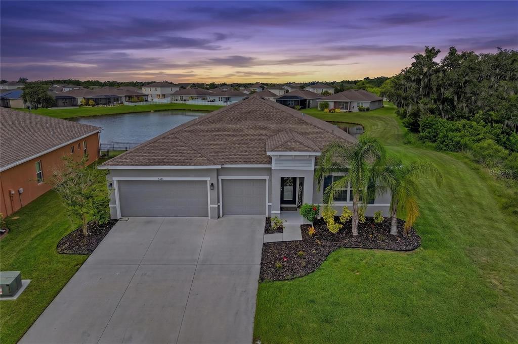 An aerial view of a single-story suburban house with a three-car garage and pond — 6421 114TH AVENUE E, PARRISH, FL