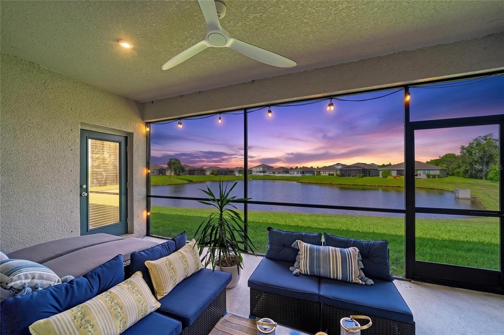 A screened-in patio features blue outdoor furniture overlooking a lake at sunset — 6421 114TH AVENUE E, PARRISH, FL