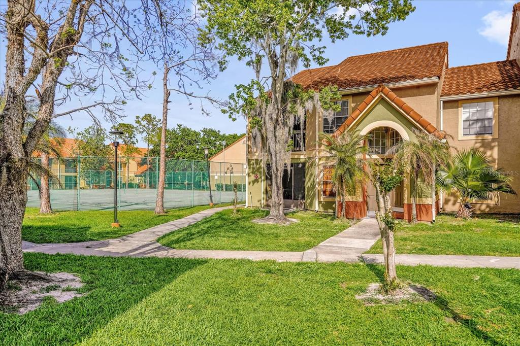 A two-story apartment building exterior with a tennis court and grassy lawn in the foreground — 409 FOUNTAINHEAD CIRCLE UNIT 236, KISSIMMEE, FL