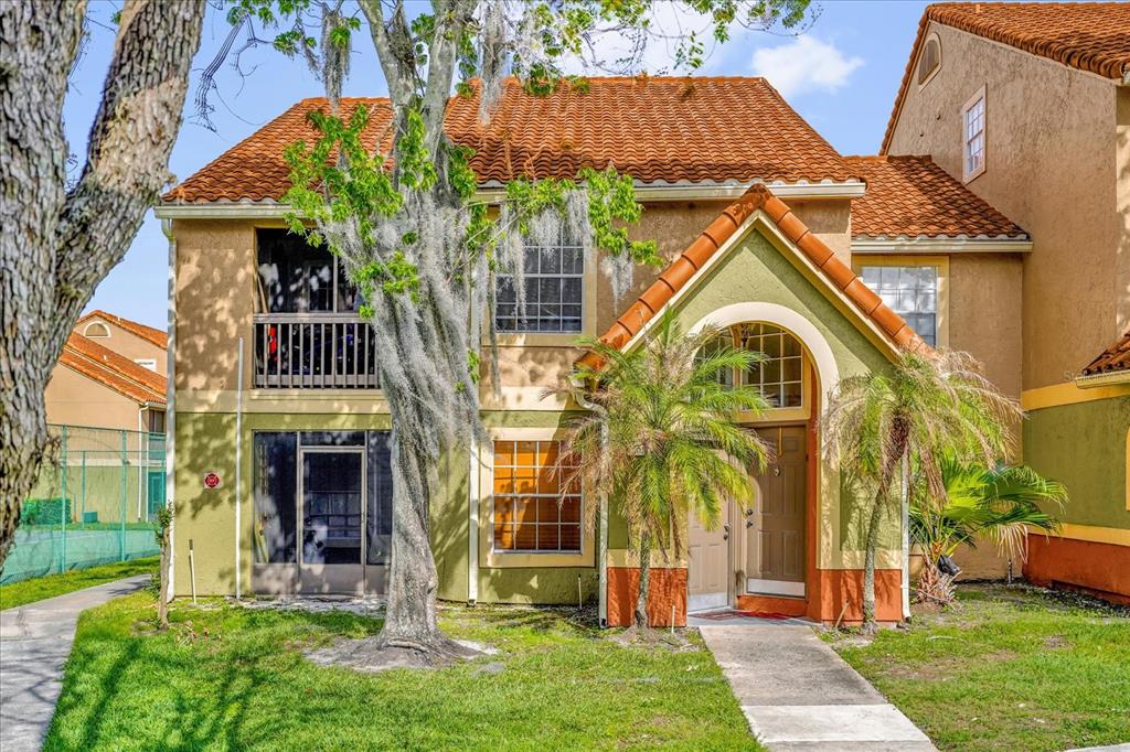 A two-story stucco townhouse with a red tile roof, screened balcony, and arched entryway — 409 FOUNTAINHEAD CIRCLE UNIT 236, KISSIMMEE, FL