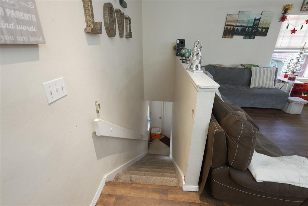 A carpeted staircase leads downward between a living area with a sofa and a wall — 409 FOUNTAINHEAD CIRCLE UNIT 236, KISSIMMEE, FL