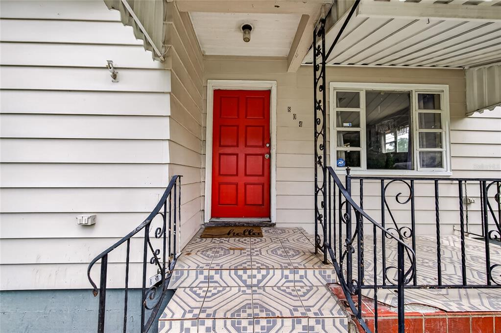 A red front door is centered on a porch with patterned tiles and metal railings — 804 E FLORA STREET, TAMPA, FL