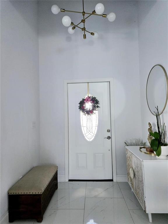 An entryway features a white door with a wreath, a chandelier, a bench, and a console — 1819 NW 21ST STREET, CAPE CORAL, FL