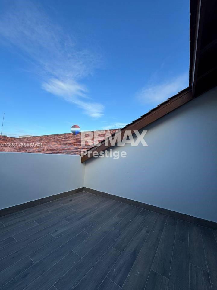 An outdoor balcony features grey wood-look tile flooring and a white wall under a clear sky — 1 La Altagracia # 0, FL