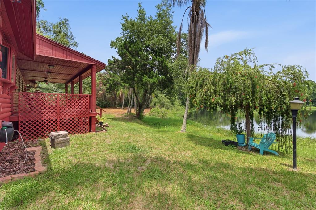A red wooden house with a porch overlooks a grassy yard and a small lake — 6409 CHISWICK COURT, NEW PORT RICHEY, FL