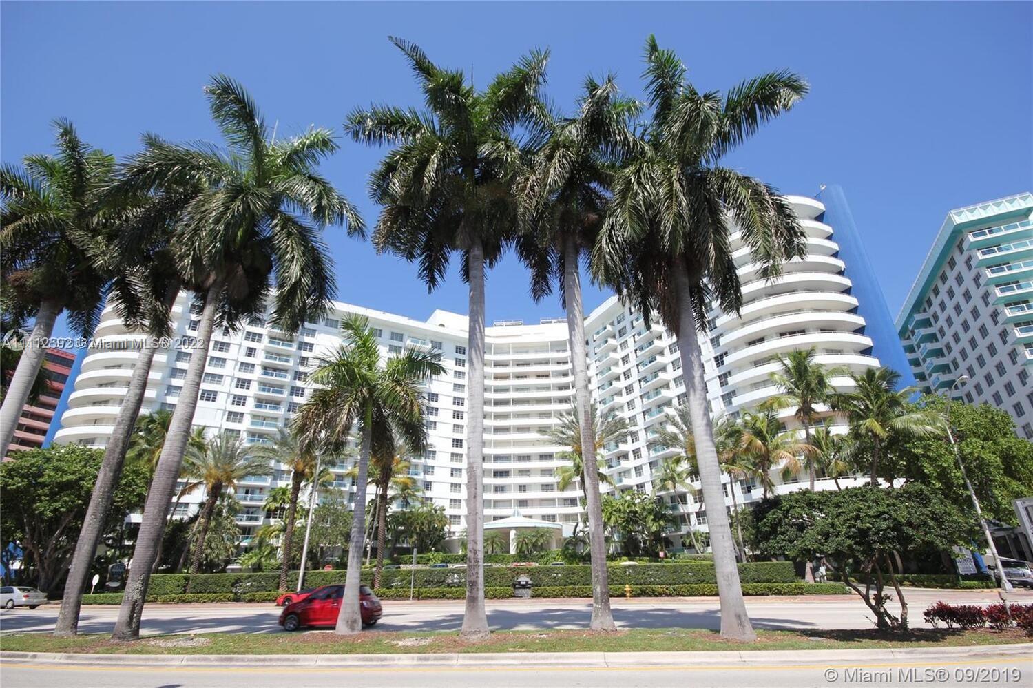 A multi-story white residential building is framed by tall palm trees under a clear sky — 5161 Collins Ave # 210, Miami Beach FL 33140, MIAMI BEACH, FL