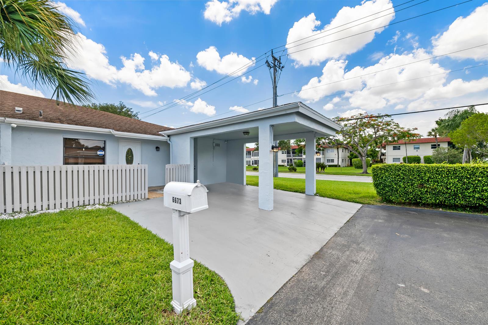 A light blue house features a covered carport, a white picket fence, and a mailbox — 6673 Moonlit Drive, Delray Beach FL 33446, DELRAY BEACH, FL