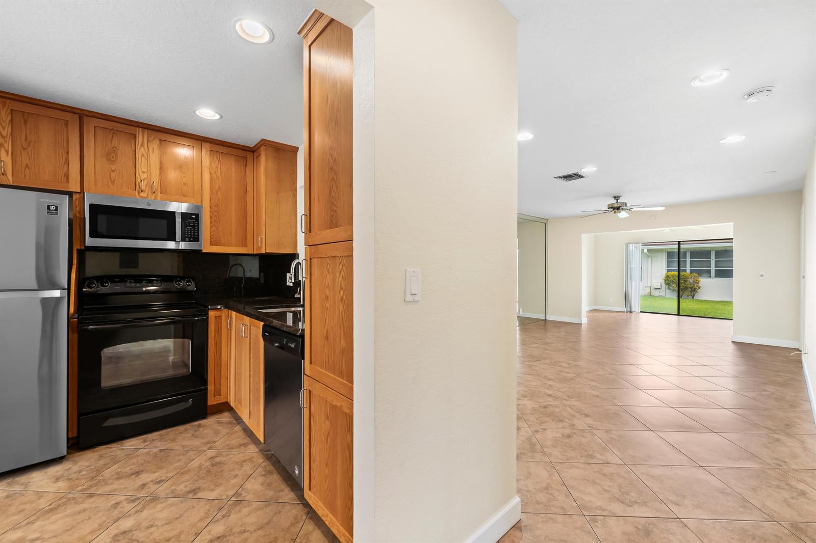 A kitchen with wood cabinets and stainless appliances opens to a tiled living area — 6673 Moonlit Drive, Delray Beach FL 33446, DELRAY BEACH, FL