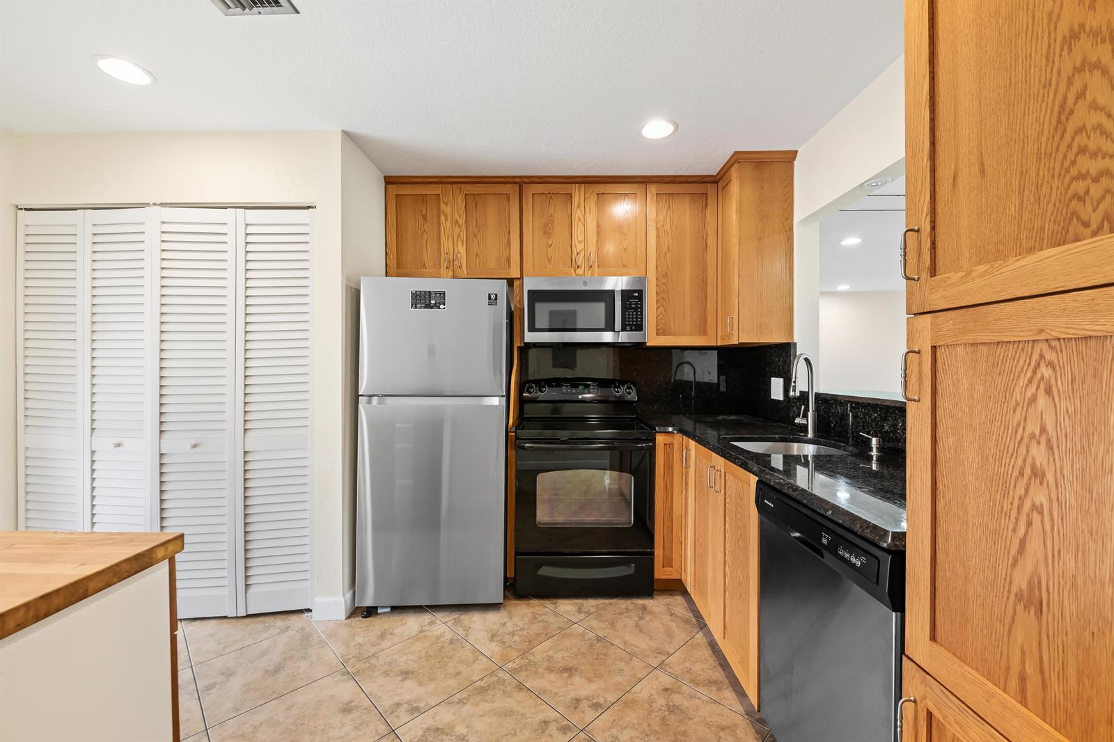 A kitchen features oak cabinets, black countertops, stainless steel appliances, and light-colored tile flooring — 6673 Moonlit Drive, Delray Beach FL 33446, DELRAY BEACH, FL