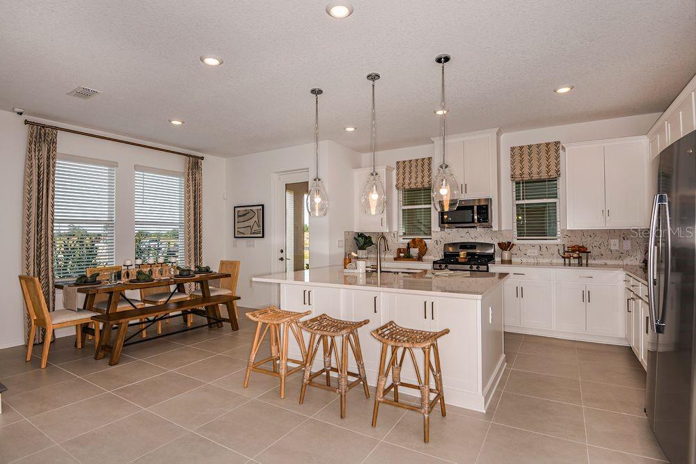 A kitchen with white cabinets, a large island with three stools, and an adjacent dining area — 14780 FIELD DAISY DRIVE, WINTER GARDEN, FL