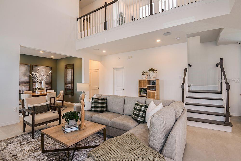 A living room with a sectional sofa, coffee table, and staircase under a high ceiling — 14780 FIELD DAISY DRIVE, WINTER GARDEN, FL
