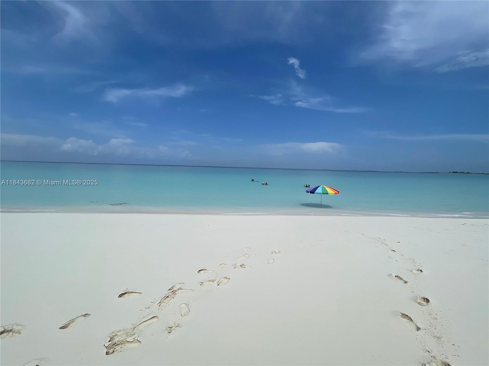 A colorful beach umbrella stands in the shallow turquoise water of a sandy beach — 6892 GREAT HARBOUR DR, BH GH24440, BH