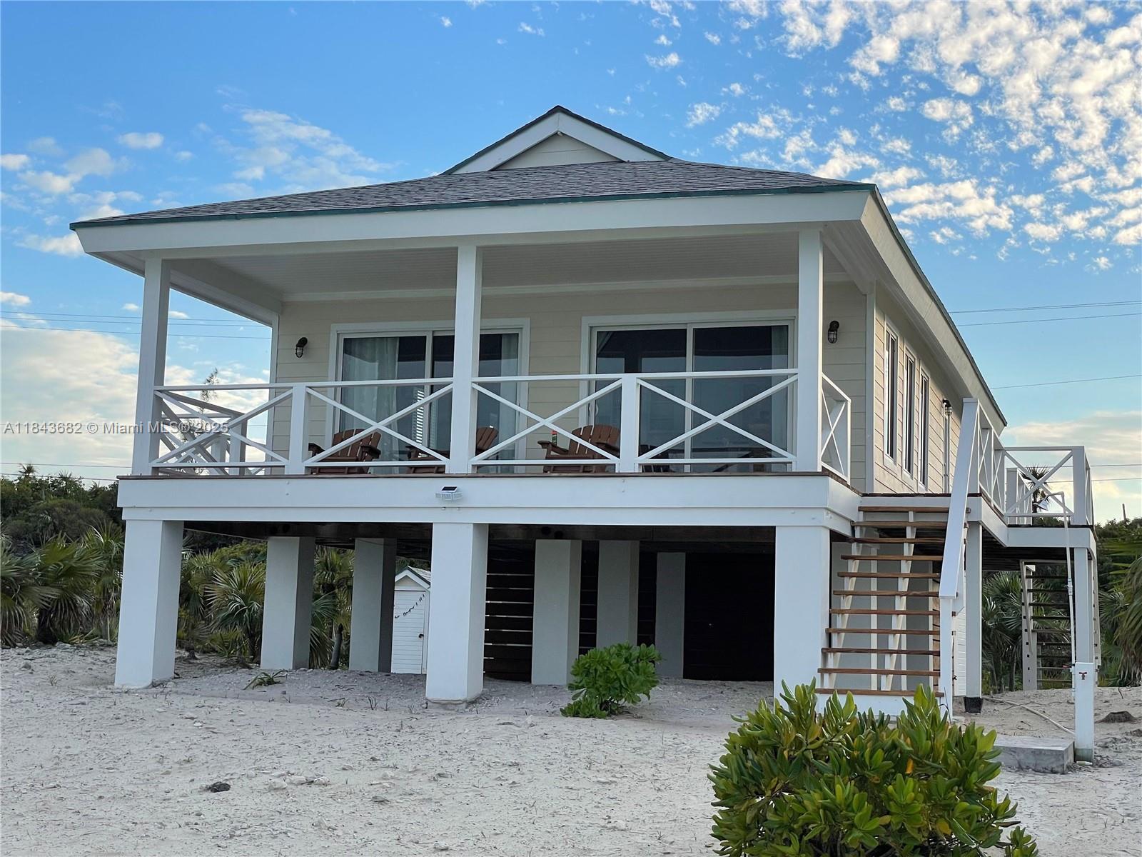 A stilt house with a large porch and wooden stairs sits on a sandy lot — 6892 GREAT HARBOUR DR, BH GH24440, BH