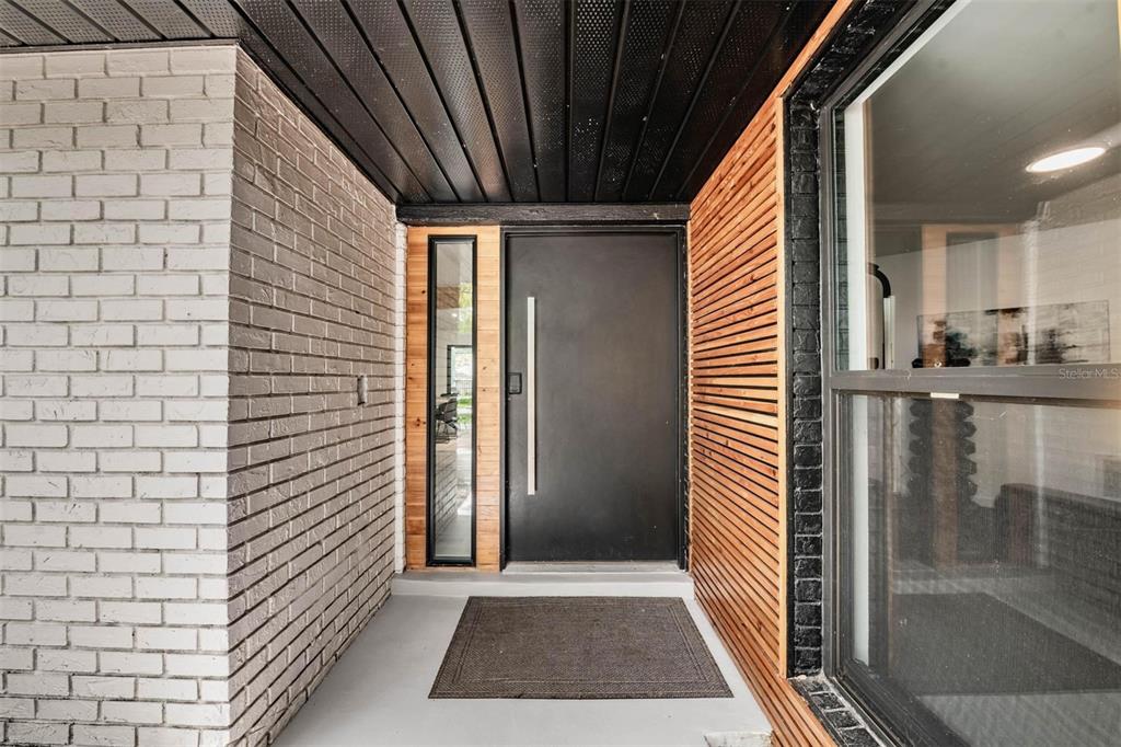 A modern entryway features a black door, wood slat siding, and a white brick wall — 848 HILLSIDE DRIVE, PALM HARBOR, FL