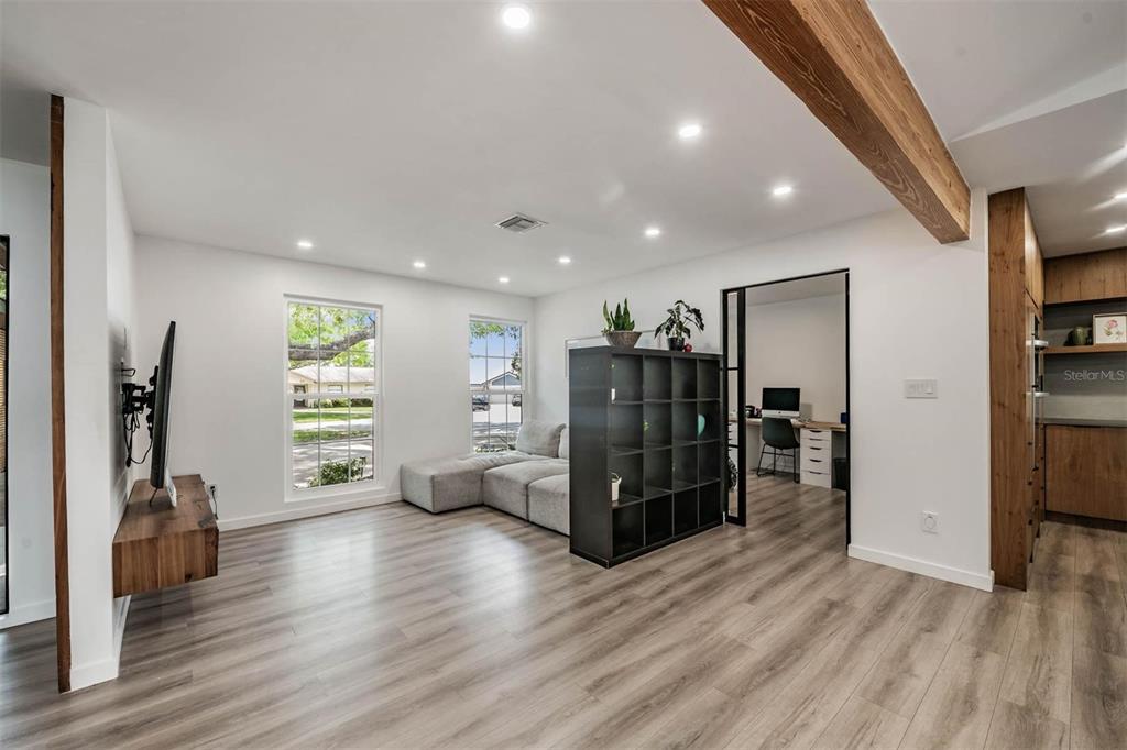 A living room with light wood floors, a black room divider, and a wooden ceiling beam — 848 HILLSIDE DRIVE, PALM HARBOR, FL
