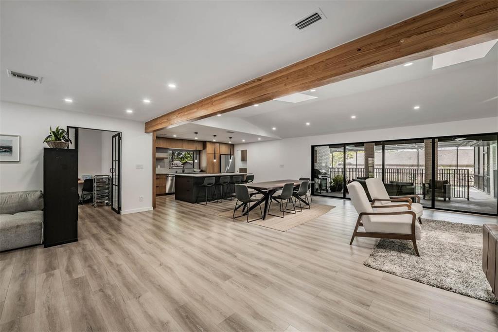 An open-concept living and dining area features wood-look flooring, a large wooden beam, and sliding doors — 848 HILLSIDE DRIVE, PALM HARBOR, FL