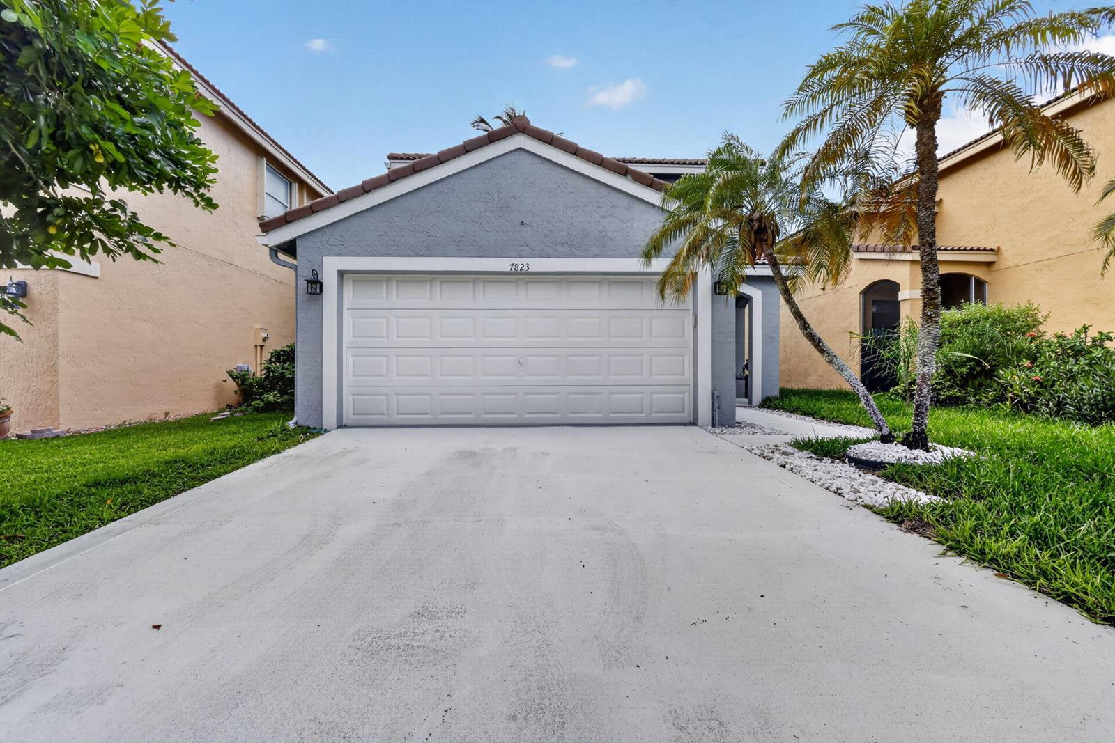 A gray house with a white garage door and a palm tree in the front yard — 7823 Springfield Lake Drive, Lake Worth FL 33467, LAKE WORTH, FL