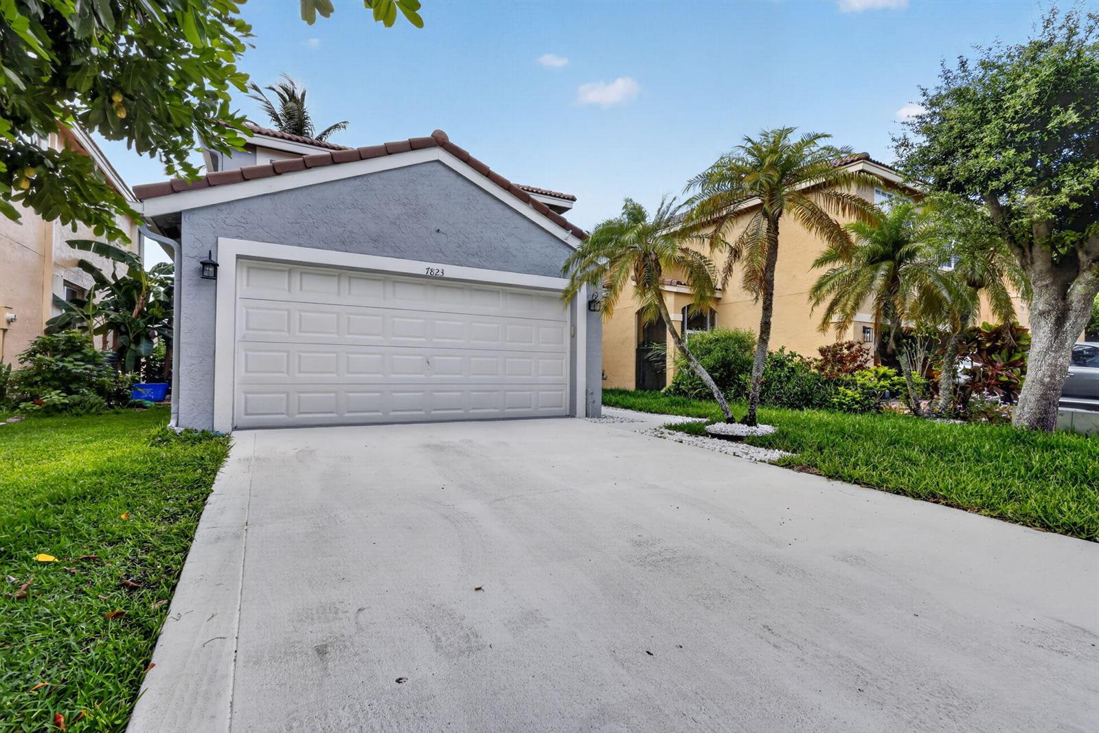 A gray house with a two-car garage and a concrete driveway under a blue sky — 7823 Springfield Lake Drive, Lake Worth FL 33467, LAKE WORTH, FL