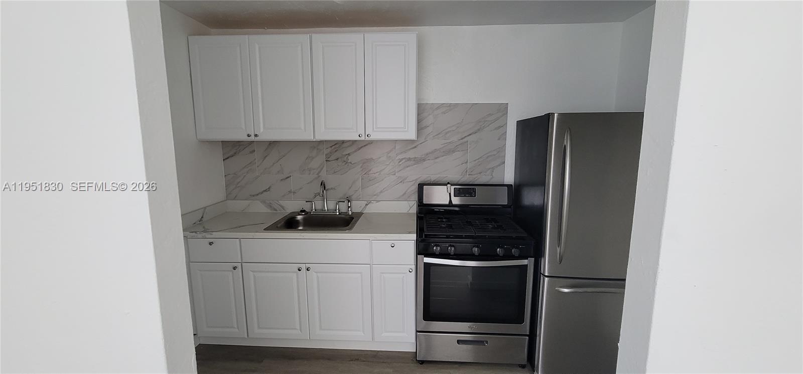 A small kitchen features white cabinets, stainless steel appliances, and a marble-patterned backsplash — 111 SW 18th Ave # 3, Miami FL 33135, MIAMI, FL