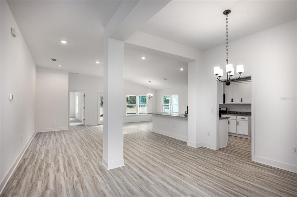An open-concept living area with light wood-look flooring, white walls, and a kitchen visible beyond — 16808 NW 178TH TERRACE, ALACHUA, FL