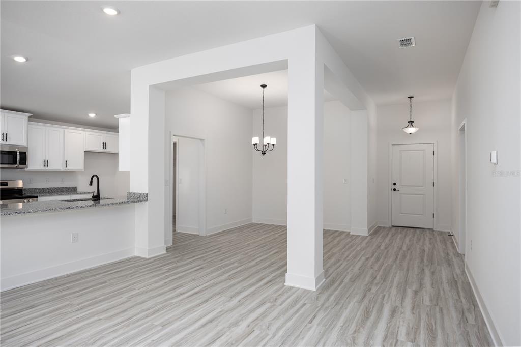 A bright, open-concept kitchen and dining area featuring white cabinetry, granite countertops, and wood-look flooring — 16808 NW 178TH TERRACE, ALACHUA, FL