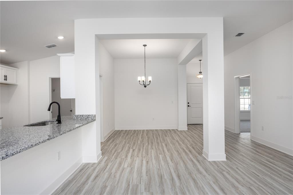 A dining area with a chandelier, light wood-look flooring, and a granite kitchen counter — 16808 NW 178TH TERRACE, ALACHUA, FL