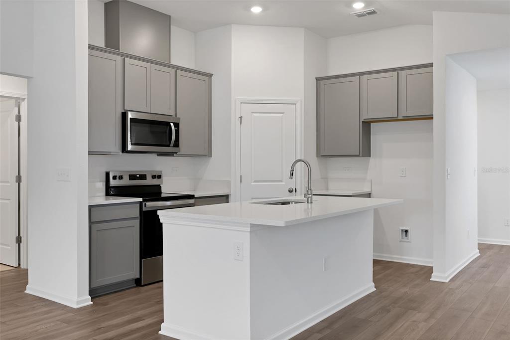 A kitchen features gray cabinets, stainless steel appliances, a white island, and light wood flooring — 5712 LAGOON CRUISE WAY, JACKSONVILLE, FL