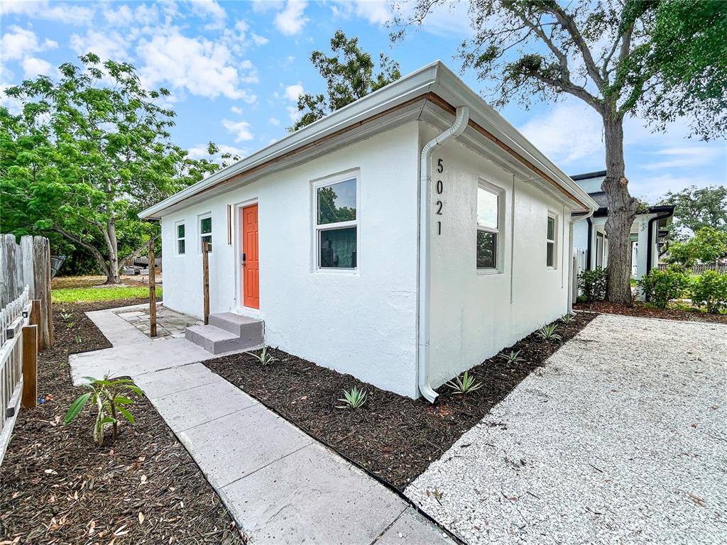 A white single-story house with an orange door and a gravel driveway — 5021 9TH AVENUE S, GULFPORT, FL