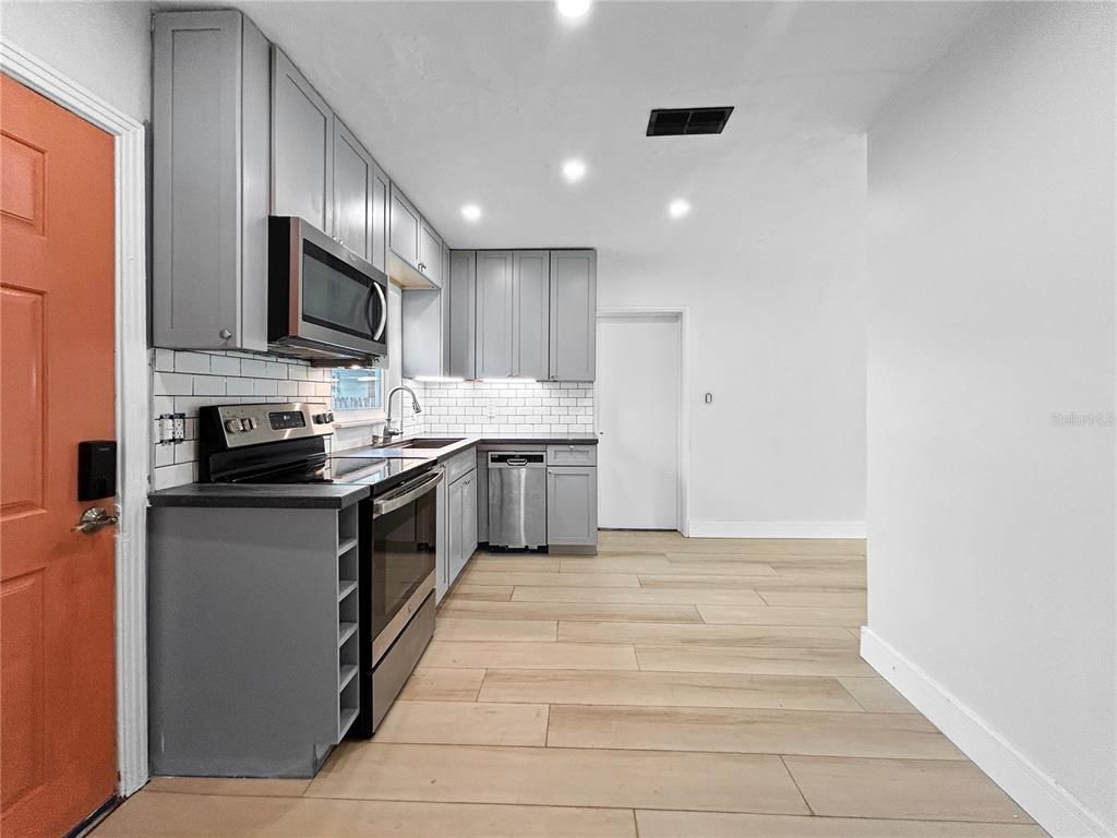 A kitchen features gray cabinets, stainless steel appliances, white subway tile backsplash, and wood-look flooring — 5021 9TH AVENUE S, GULFPORT, FL